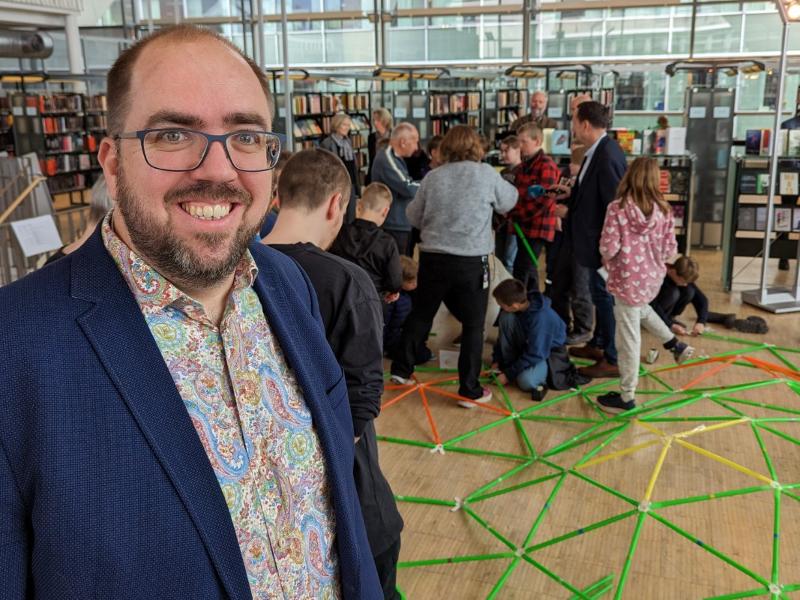 Cordian Riener Abel bibliotek.jpg Ein mann smilar og ser i kamera. Ungar leikar i bakgrunnen.
